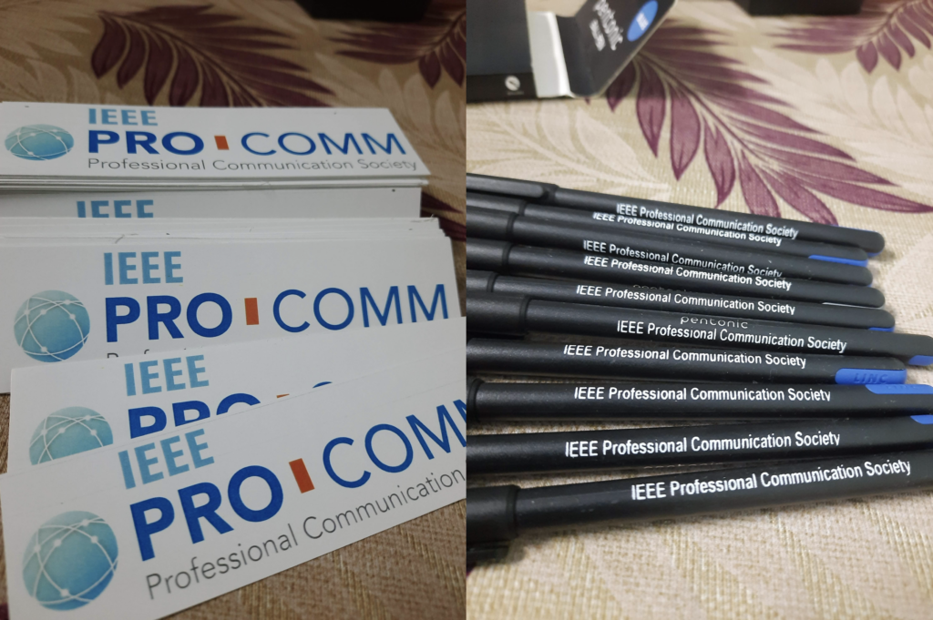 Photo of IEEE ProComm outreach gifts provided at this event. On the left, we see IEEE ProComm branded stickers and on the right,  we see IEEE ProComm branded pens.